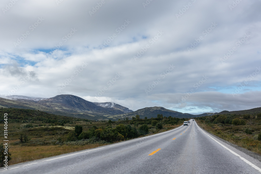 Fototapeta premium Mountains in Norway road epic scenic sky, way, clouds view. Traveling by car, driving nature tourism. Dramatic skyscape northern scandinavian sky