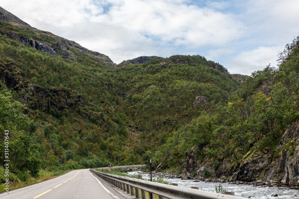 Mountains in Norway road near rocky river epic scenic sky, way, clouds view. Traveling by car, driving nature tourism. Dramatic skyscape northern scandinavian sky Mountains in Norway road near rocky river epic scenic sky, way, clouds view. Traveling by car, driving nature tourism. Dramatic skyscape northern scandinavian sky