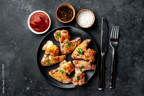 grilled chicken wings on a black plate with spices and herbs on a stone background with copy space for your text