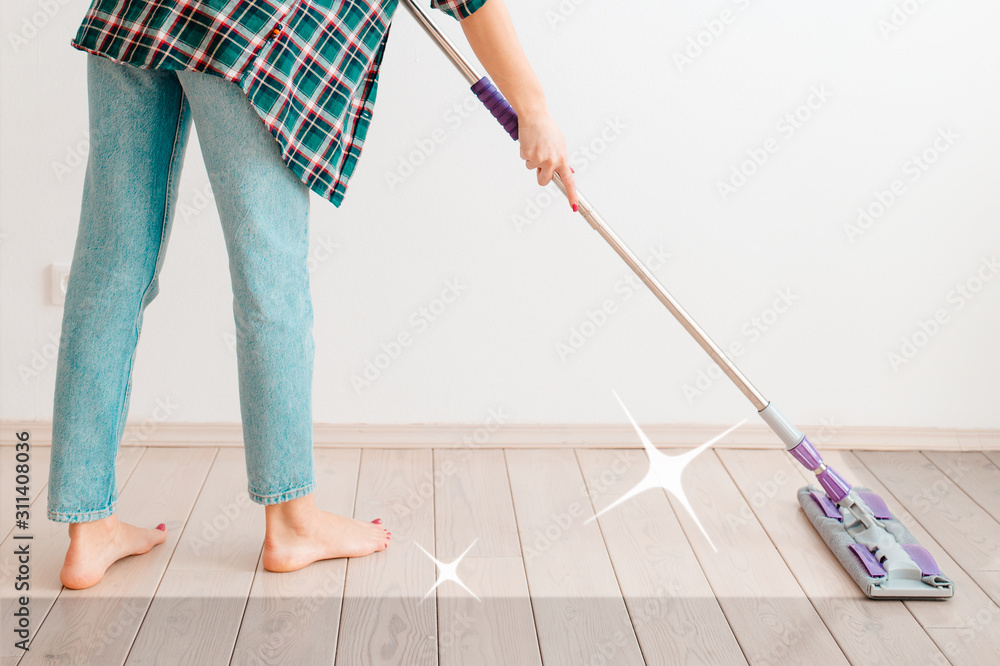 The concept of cleaning. Woman in casual clothes washing floors. There is a white wall in the background. There's a clean cleaning trail on the floor. Copy space The concept of cleaning. Woman in casual clothes washing floors. There is a white wall in the background. There's a clean cleaning trail on the floor. Copy space
