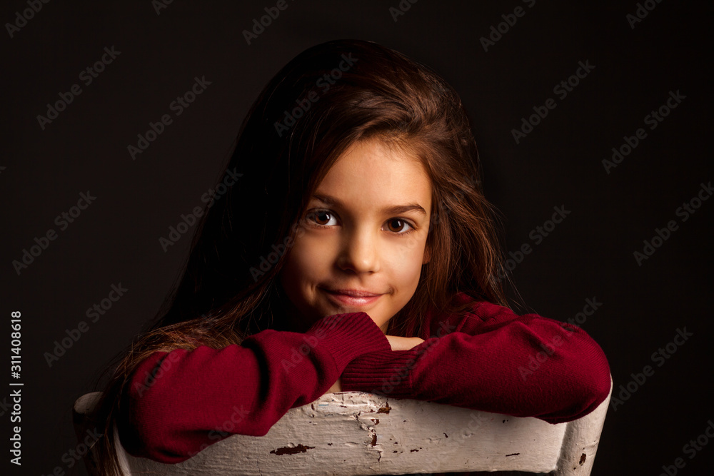 portrait of a girl with long brown hair in a red sweater on a white chair on a black background portrait of a girl with long brown hair in a red sweater on a white chair on a black background