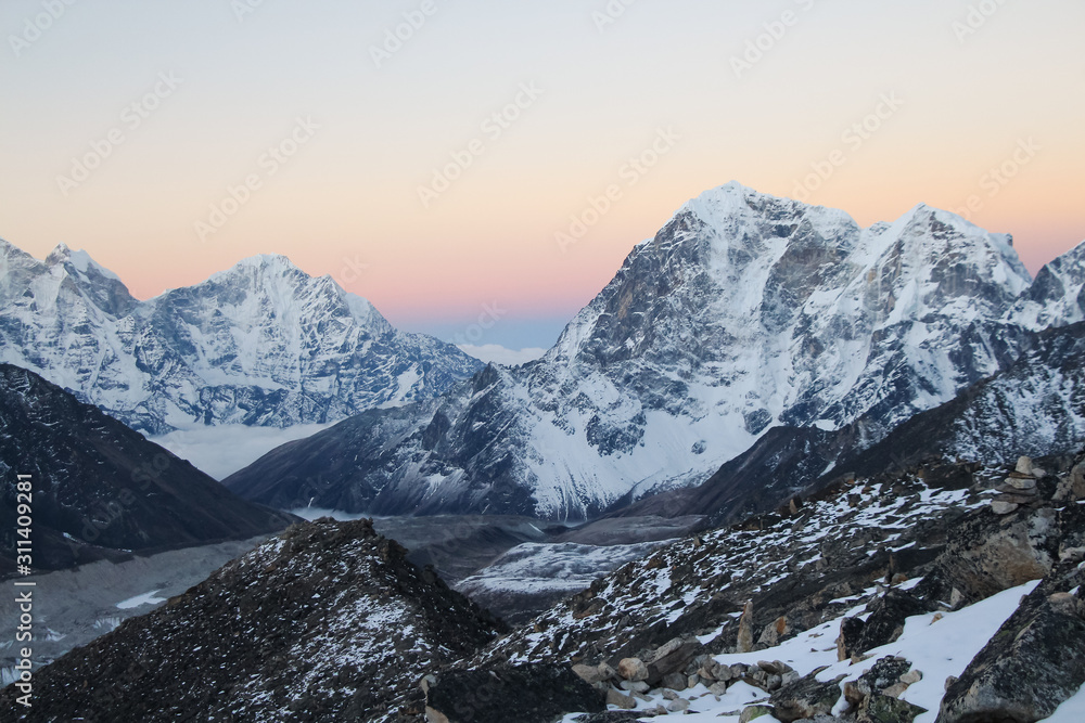 Taboche and Kangtega mountain peaks rises above Khumbu glacier and valley covered with clouds in the early morning in Himalayas. Theme of trekking in Nepal. Clear sunrise sky.