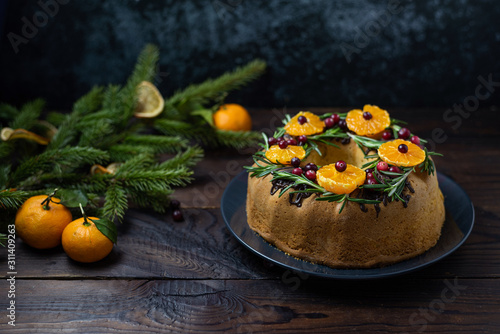 Tangerine ring cake decorated with sliced mandarines, cranberries and rosemary on dark blue background with copy space.