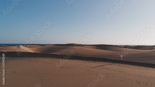 Aerial view - an attractive girl walks along the sand in the rays of the setting sun  Maspalomas  Gran Canaria