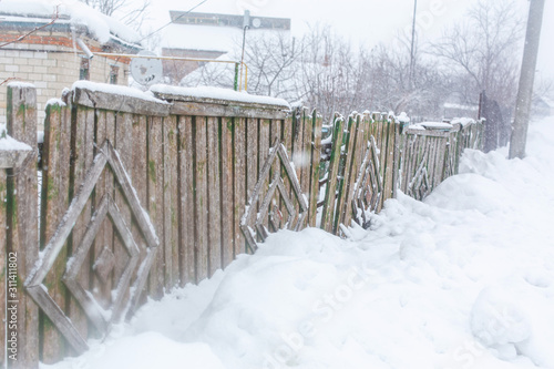 Winter old dilapidated rickety fence of wooden boards. A snow blizzard
