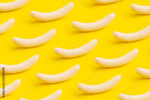 Ripe peeled bananas pattern on yellow background, minimal diet concept.