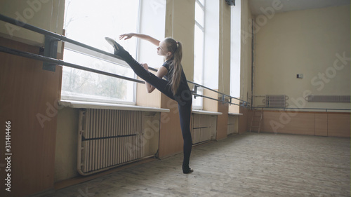 Young graceful female ballet dancer in training clothes exercising in ballet class