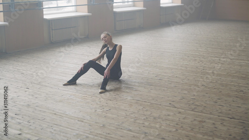 Elegant ballet dancer stretching in the lighted room