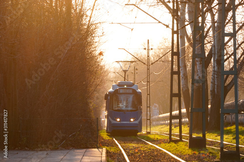 city trams in rays of the sunset soft bright back-light sun, glare on the wires, trams and rails. light in the frame. railway in the environment of the city Park near the forest, rails in the grass.