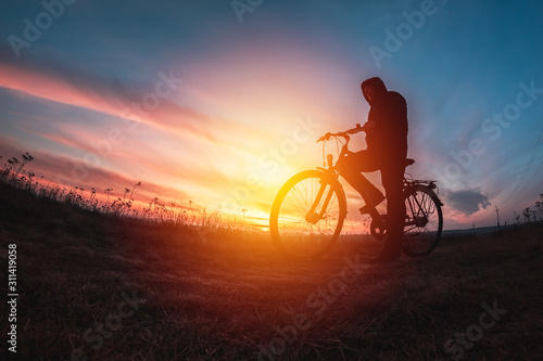 man with bicycle on the mountain looks at sunset