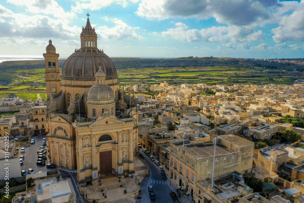 Obraz premium Aerial view oа St. John Baptist Church. Countryside of Gozo island, cloudy blue sky. Malta country