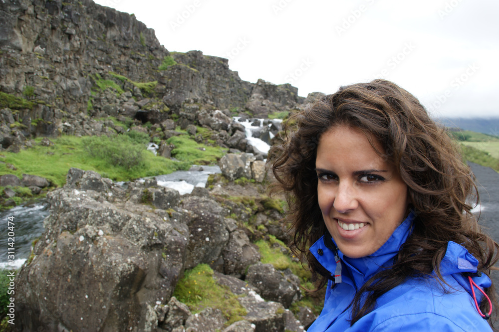 Portrait of a smiling woman with a blue raincoat on mountain hike in Thingvellir (Iceland)