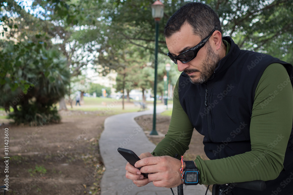 Man looking at the smartphone while resting during his bike ride. Man looking at the smartphone while resting during his bike ride.