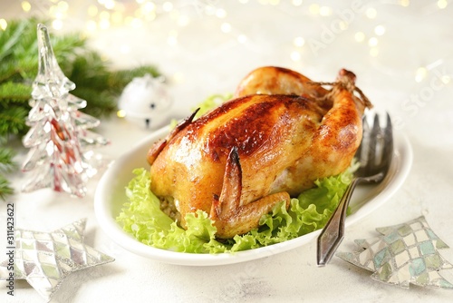 Roasted whole chicken on lettuce leaves. Christmas light background.