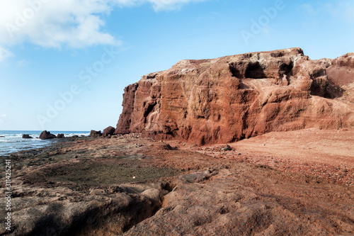 Dramatic red coloured cliffs on the coast of Montana Roja mountain near El Medano, Tenerife, Canary Islands, Spain, sunny summer day