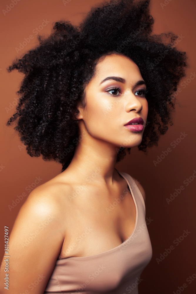 pretty young african american woman with curly hair posing cheerful gesturing on brown background, lifestyle people concept pretty young african american woman with curly hair posing cheerful gesturing on brown background, lifestyle people concept