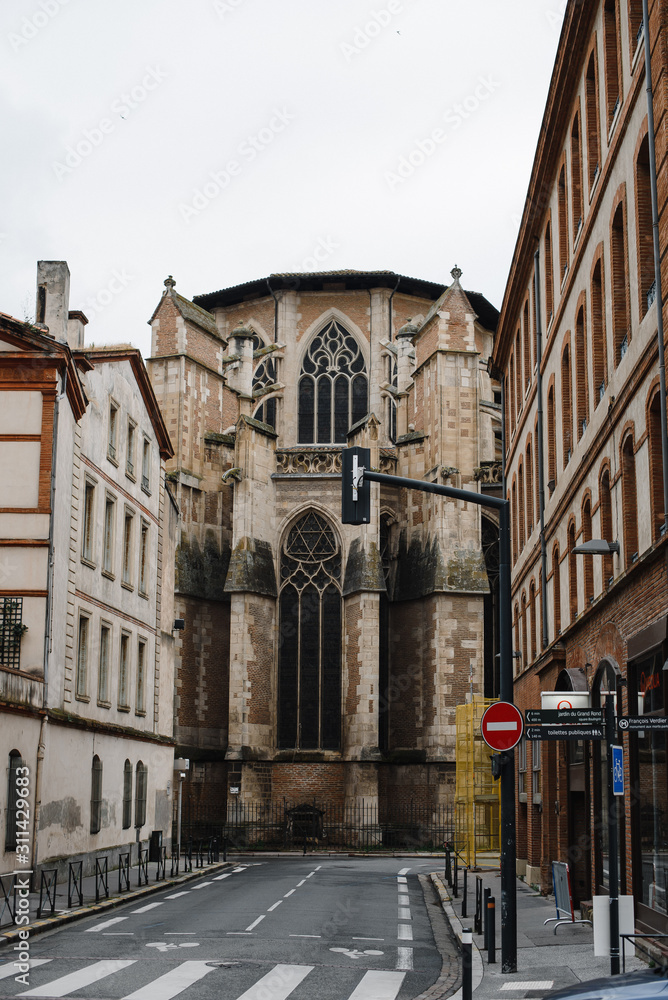 Antique Gothic Church Tower on the narrow streets of Toulouse France. Photography of a European urban view with a modern road and an old medieval building with exterior decoration.
