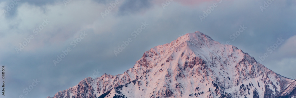 Plakat Snowy mountain top illuminated by sunset with dramatic clouds in background