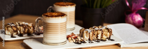 Banner size image of two cups of Hot latte with baked caramel crust and sweet roll with banana and strawberry on the wooden table in coffe-shop. Coffee concept