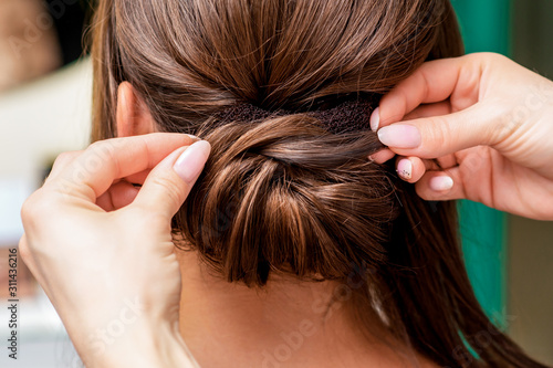Rear view of hairdresser hands making hairstyle for woman in beauty salon, close up.