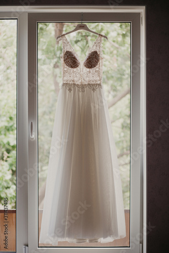 Wedding dress on hanger near window in the bride room. On her wedding day