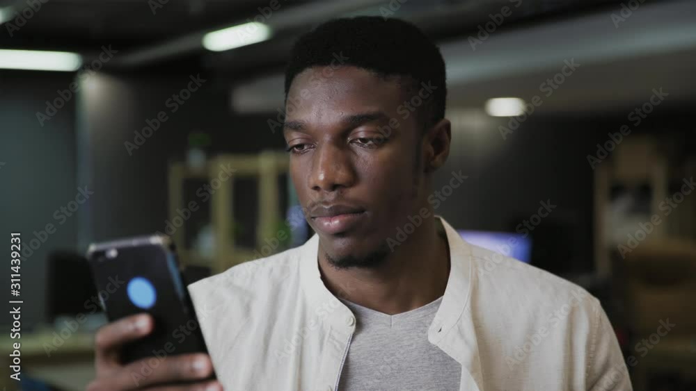 Young african man holding smartphone device texting sms message and drinking coffee or tea at a modern office Young african man holding smartphone device texting sms message and drinking coffee or tea at a modern office