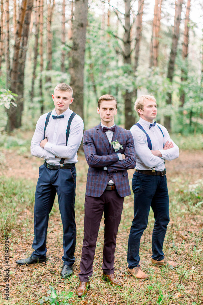 Happy handsome groom and groomsmen posing and smiling, standing on the background of pine forest