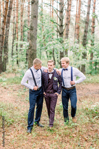 Handsome groom with stylish groomsmen walking in the forest and having fun on a wedding day.