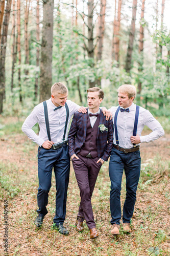 Handsome groom walking with his friends groomsmen in the pine forest on a wedding day © sofiko14