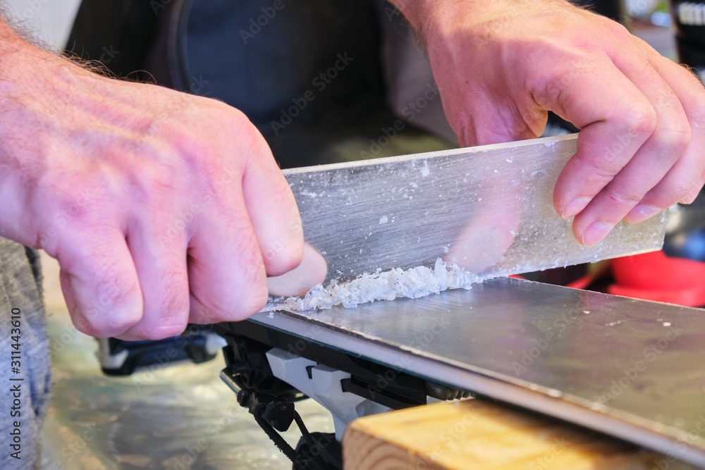 Removing excess wax from ski base using a plexi scraper - focus on the wax. Preparing the base of a ski before brushing - Ski tuning and maintenance concept.
