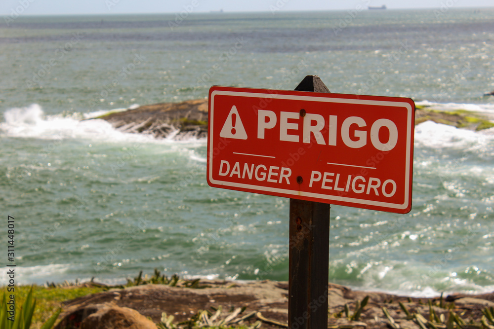 Danger red sign, in portuguese, spanish and english, by the sea