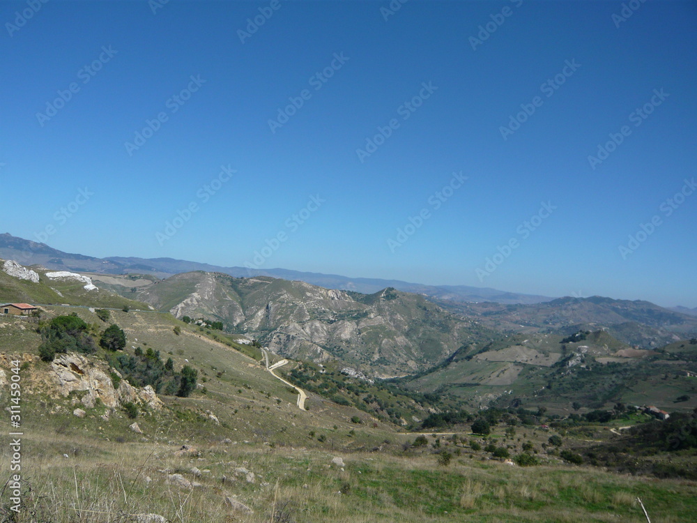 Winding road to  Enna, Sicily - Panorama  of hills, outcroppings, mountains, house, sunshine everywhere, blue sky 