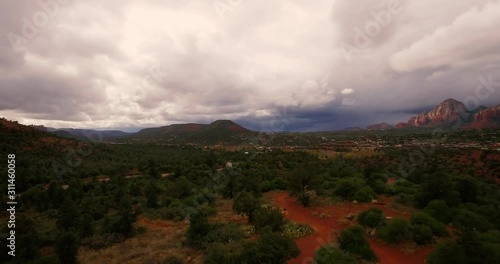 Aerial assent in the light rain from juniper tree forest in Coconino National Forest to a view of the grand red rock formations of Sedona, Arizona, photo