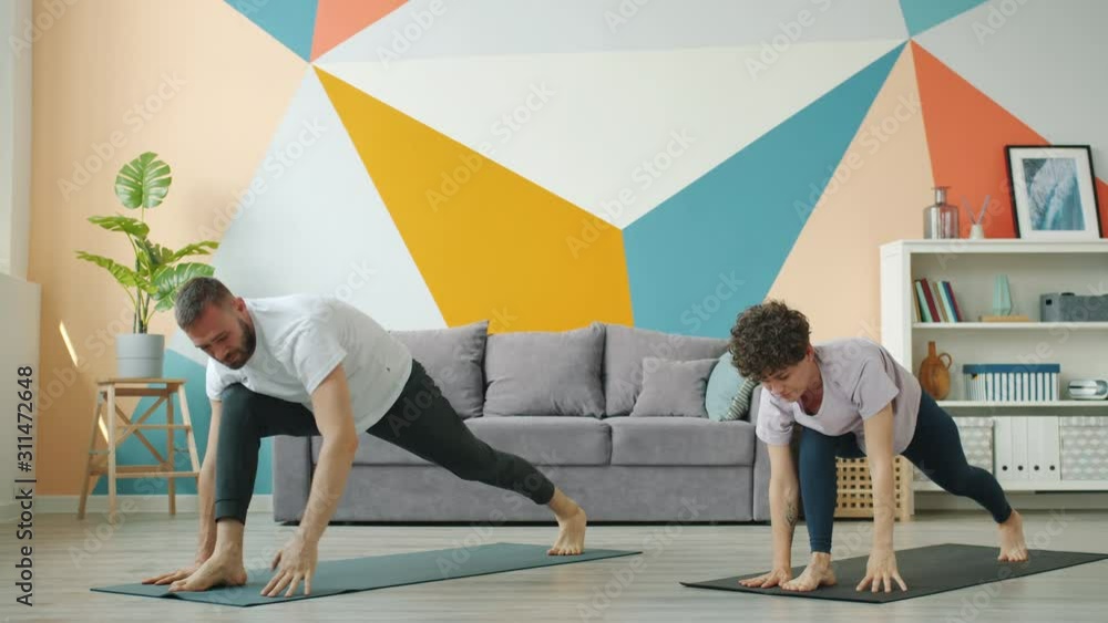 Woman and man are working out at home doing yoga together synchronously on mats caring for body health. Modern people, sports and apartment concept. Woman and man are working out at home doing yoga together synchronously on mats caring for body health. Modern people, sports and apartment concept.