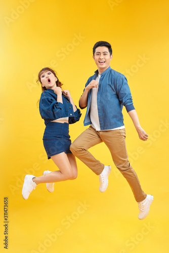 Full length body size photo funky she her he him his pair jumping high raised fists yell scream shout loud wear casual jeans denim white t-shirts isolated yellow background © makistock