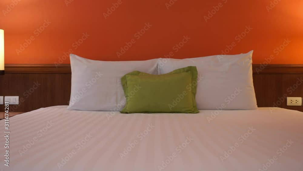 Hotel room interior with white clean bed with two white pillows and a green cusion in the middle, panning shot from left to right. Hotel room interior with white clean bed with two white pillows and a green cusion in the middle, panning shot from left to right.