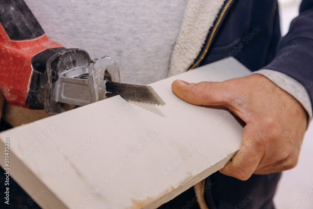 A man is cutting a board of wood with a jigsaw detail of a cutting wooden board with saw dust.