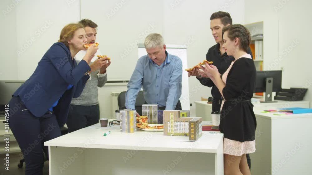 Office workers take slices of pizza from the table with model of houses Office workers take slices of pizza from the table with model of houses