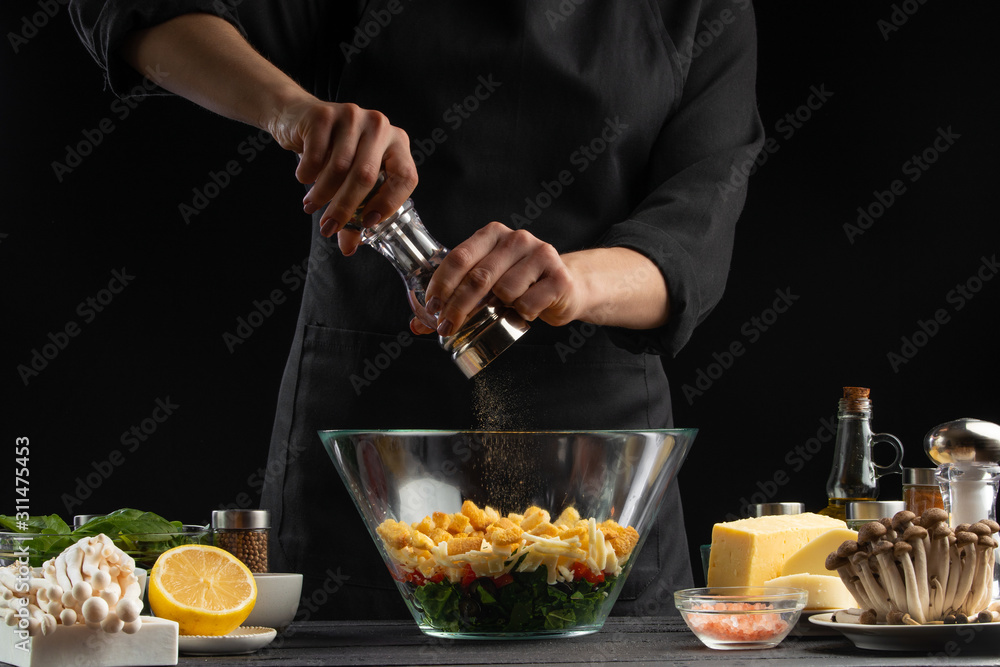 professional chef cooks a fresh and healthy salad, salting it with salt hodgepodge, Freezing in motion.Organic and wholesome food.Healthy nutrition and vitamins Advertising photo on black background professional chef cooks a fresh and healthy salad, salting it with salt hodgepodge, Freezing in motion.Organic and wholesome food.Healthy nutrition and vitamins Advertising photo on black background