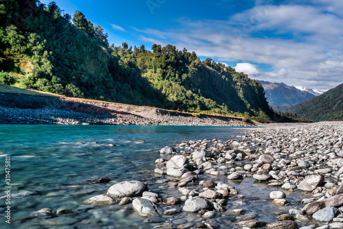 Crystal clear blue water of the swift flowing Whataroa river weaving its way into the Southern Alps on New Zealand's West Coast