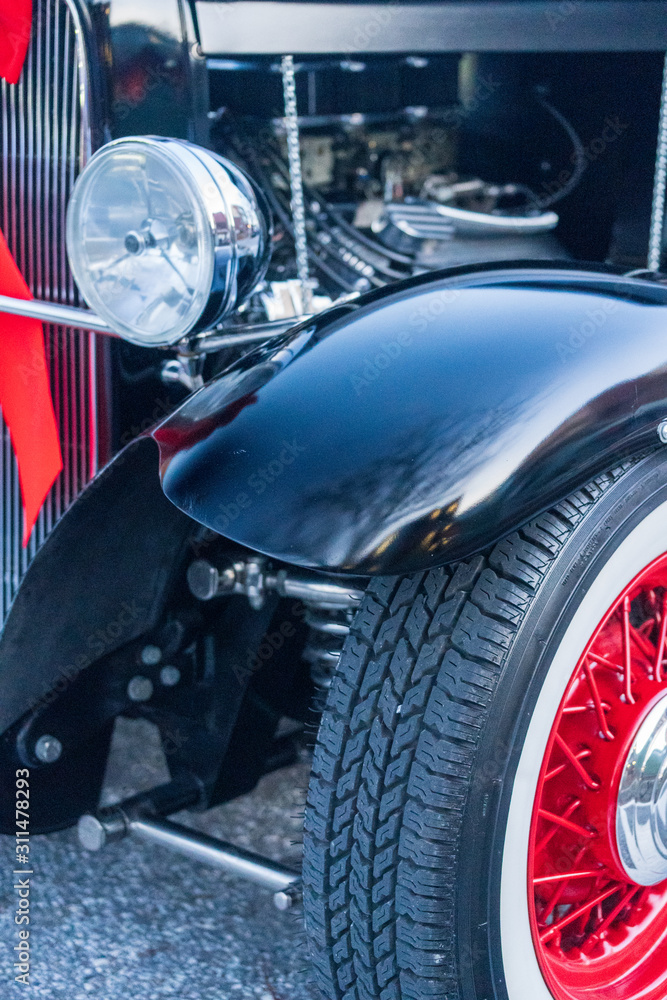 Head light and fender of black antique car with red accents.