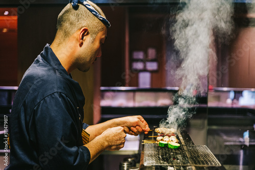 Photography Japanese Yakitori Chef is grilling chicken marinated with ginger, garlic and soy sauce and cucumber with a lot of smoke