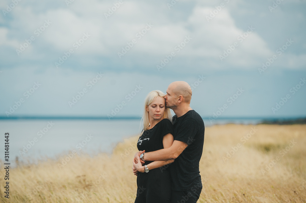 Romantic view of couple in black clothes when they kiss on the edge of the rocky coast of the Baltic sea.