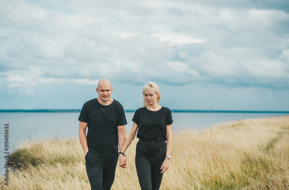 Romantic view of couple in black clothes when they walking on the edge of the rocky coast of the Baltic sea.