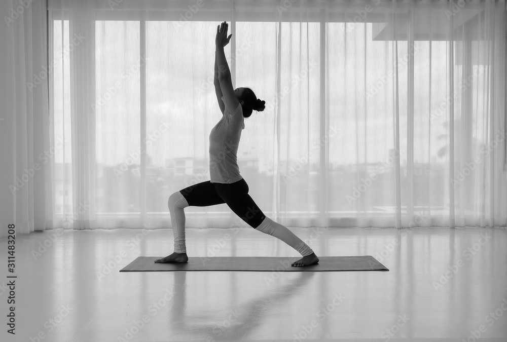 Side view portrait of beautiful young woman doing yoga or pilates exercise. Standing in Warrior one pose, Virabhadrasana, working out,In the white room indoor full length Side view portrait of beautiful young woman doing yoga or pilates exercise. Standing in Warrior one pose, Virabhadrasana, working out,In the white room indoor full length