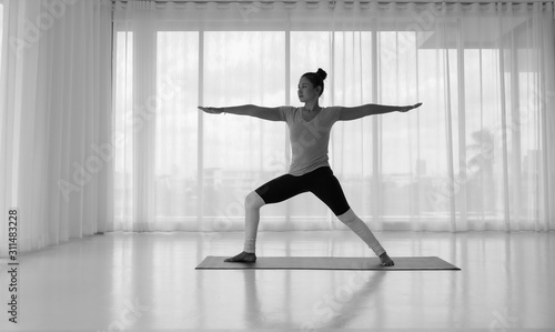 Asian woman practicing yoga, standing in Warrior two exercise, Virabhadrasana II pose on mat, working out wearing sportswear for yoga , full length , white yoga, Concept of healing body and spirit.