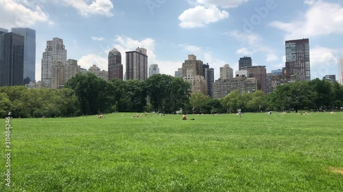 NEW YORK - JUNE 28, 2019: Crowded Central Park Sheep Meadow MANHATTAN public park. People sit, picnic, play games sports, talk, community, rest, relax, meditate, and play spikeball, grass, blue sky photo