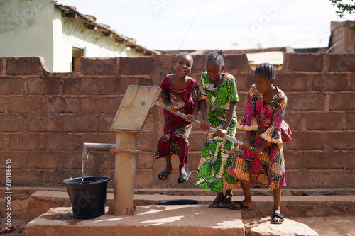 Three Little African Girls Having Fun While Pumping Water At The Borehole photo