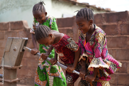 Three Smiling Little African Girls Busy Fetching Water At The Village Pump