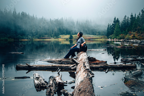 An Asian woman sitting down and looking up reflecting and pondering in the middle of foggy mountain at a lake